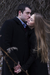 young couple in black coats kissing in park