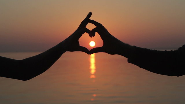 Hands make heart at sunset