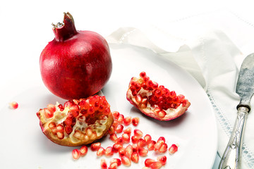 pomegranate whole and pieces with grains on a white plate