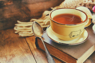 Cup of tea with old book and a warm scarf on wooden table
