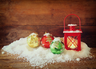 christmas background with red lantern, bauble and snow over wooden background
