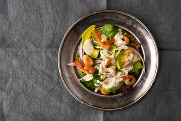 Shrimps and avocado salad on the vintage metal plate on the grey tablecloth