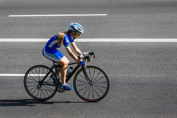 Female cyclist rides a racing bike on road - obrazy, fototapety, plakaty