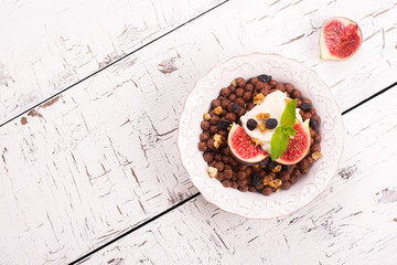 Healthy breakfast: bowl of chocolate balls with yoghurt and fresh figs on white wooden table. Selective focus