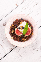 Healthy breakfast: bowl of chocolate balls with yoghurt and fresh figs on white wooden table. Selective focus