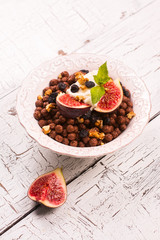 Healthy breakfast: bowl of chocolate balls with yoghurt and fresh figs on white wooden table. Selective focus