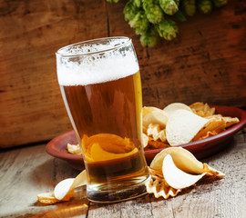 large glass of light beer and potato chips on a wooden backgroun