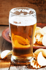 large glass of light beer and potato chips on a wooden backgroun