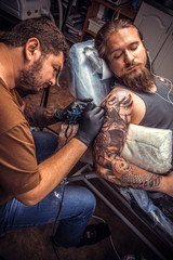 Fototapeta premium Professional tattooer showing process of making a tattoo in tattoo parlor