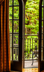 Open French doors onto a balcony with a view of leafy green trees