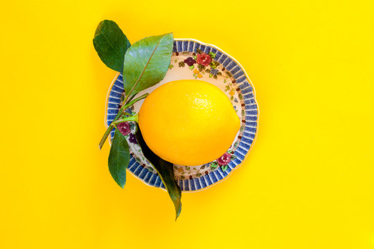 Fresh whole lemon on a vintage china plate with yellow background. Top view.