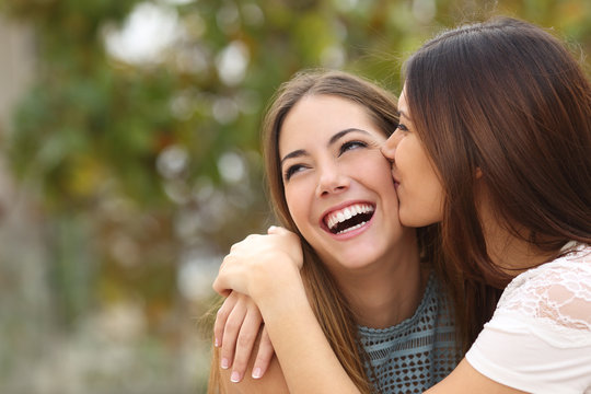 Two funny women friends laughing and kissing