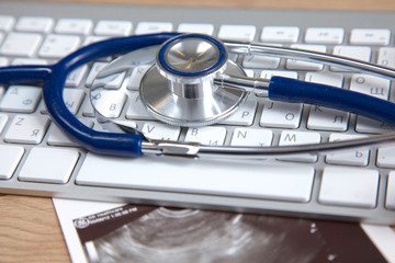 A medical stethoscope near a laptop on a wooden table, on white