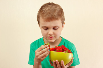 Little boy takes a fresh strawberry from the bowl