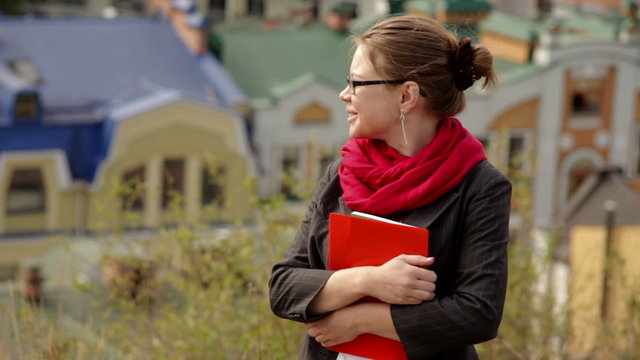 beautiful woman in glasses with red folder against summer buildings

