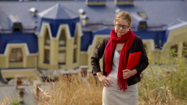 beautiful woman in glasses with red folder against summer buildings
