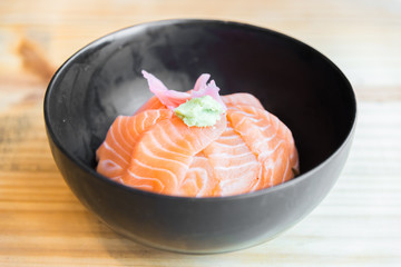Japanese Rice with salmon sashimi on top in black bowl