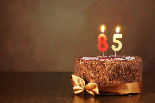 Birthday chocolate cake with burning candles as a number eighty five on brown background