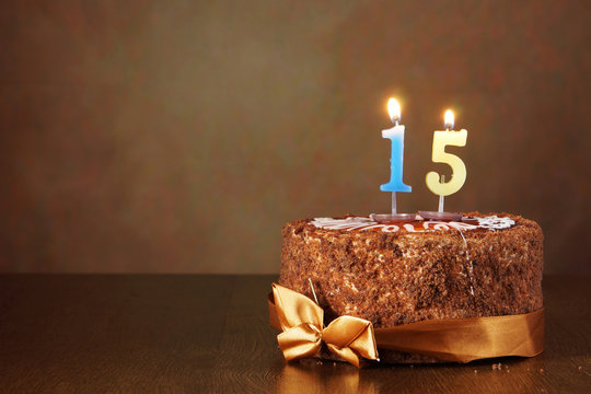 Birthday chocolate cake with burning candles as a number fifteen on brown background