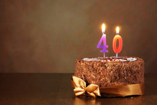 Birthday chocolate cake with burning candles as a number forty on brown background