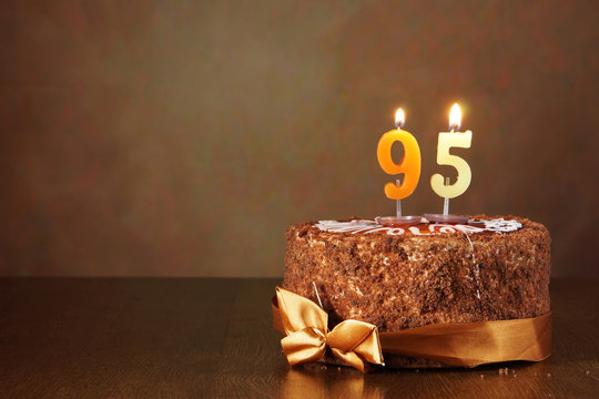Birthday chocolate cake with burning candles as a number ninety five on brown background