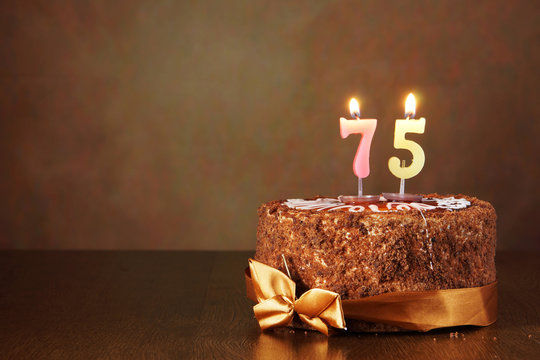 Birthday chocolate cake with burning candles as a number seventy five on brown background