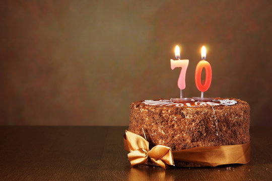 Birthday chocolate cake with burning candles as a number seventy on brown background