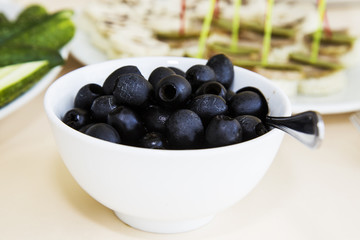 Black olives in a white Cup. The food on the table, a festive table setting, snacks, a dish for the Banquet, health food, Breakfast and lunch, large olives.
