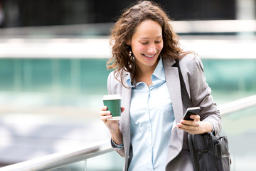 Fototapeta premium Young attractive business woman using smartphone drinking coffee