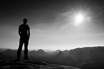 Alone man in red cap on peak of sharp peak in rock empires park and watching over the misty and...