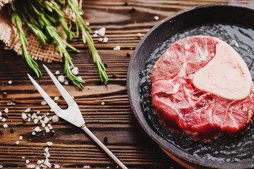 
raw meat with salt , pepper and spices fried in hot oil in a frying pan on a wooden background