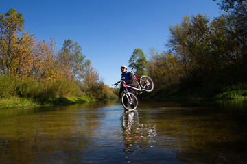 Naklejka premium Young athlete crossing rocky terrain with bicycle in his hands