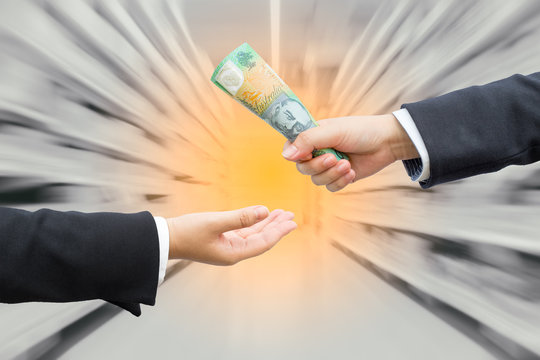 Hands of businessman passing Australian dollar (AUD) banknote with blurred supermarket background.