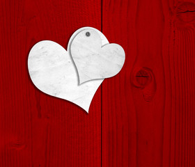 Conceptual two white old paper vintage hearts on red wood