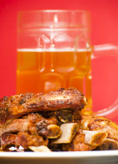 Roasted pork ribs on a white plate with a pitcher of beer next