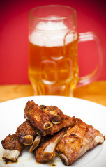 Roasted pork ribs on a white plate with a pitcher of beer next