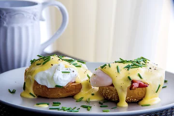 Foto auf Leinwand Eggs Benedict- toasted muffins, ham, poached eggs, and delicious buttery hollandaise sauce © proxima13