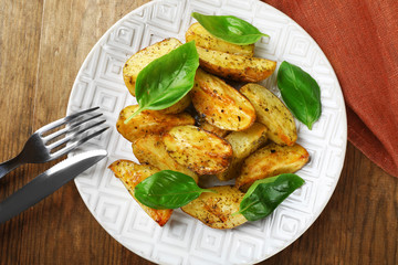 Baked potatoes with basil leaves in white plate on wooden table, top view