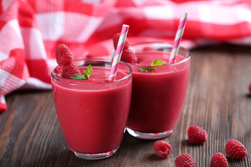 Glasses of raspberry milk shake with berries on wooden table close up