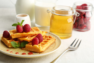 Sweet homemade waffles with fresh raspberries on plate, on light background