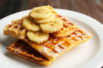 Sweet homemade waffles with sliced banana on plate, on light background