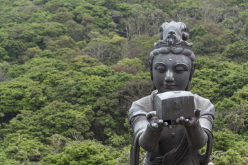 Fototapeta na wymiar Buddhistic statue making offerings to the Tian Tan Buddha in Hong Kong, against a background of lush trees