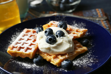 Sweet homemade waffles with blueberries and cream on plate, on dark wooden background