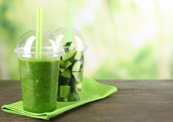 Green vegetable and fruit salad and healthy fresh drink in plastic cups on bright background. Colorful diet concept