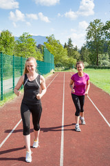 Obraz premium Zwei Frauen Lauf auf Kurs zusammen und freundliches Rennen - Blonde Frau schlägt brünette Frau im Rennen auf einer Bahn