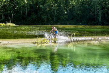 Obraz na płótnie Canvas cyclist rides a bicycle across the river at the ford