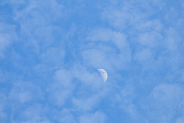Some clouds and little half moon in the blue sky.