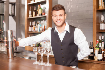Cheerful young barman is making cocktails in bar