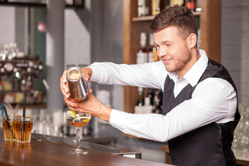 Cheerful young barman is making cocktail in bar