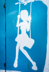 Moscow, Russia - September 27, 2015: a blue and white silhoette of a painted person on the garage wall. Girl swinging.